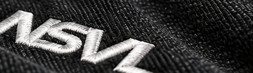Illustration: close-up of the NSVL mark embroidered in paper-white thread on charcoal fabric.