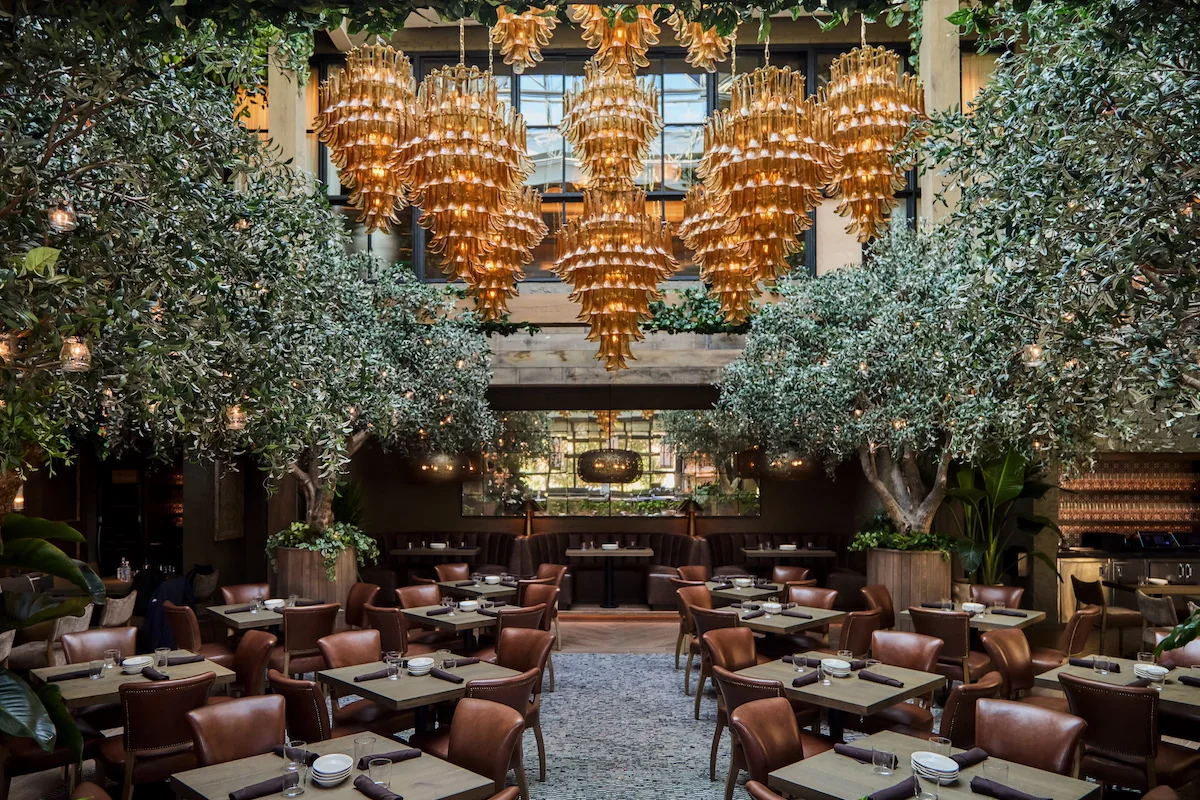 The two-story dining room at Aba Nashville with olive trees and amber glass chandeliers.