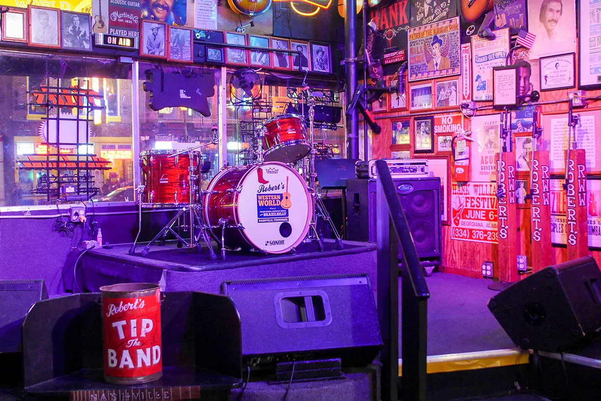 Stage interior at Robert's Western World with drum kit branding, neon lighting, and memorabilia-lined walls.